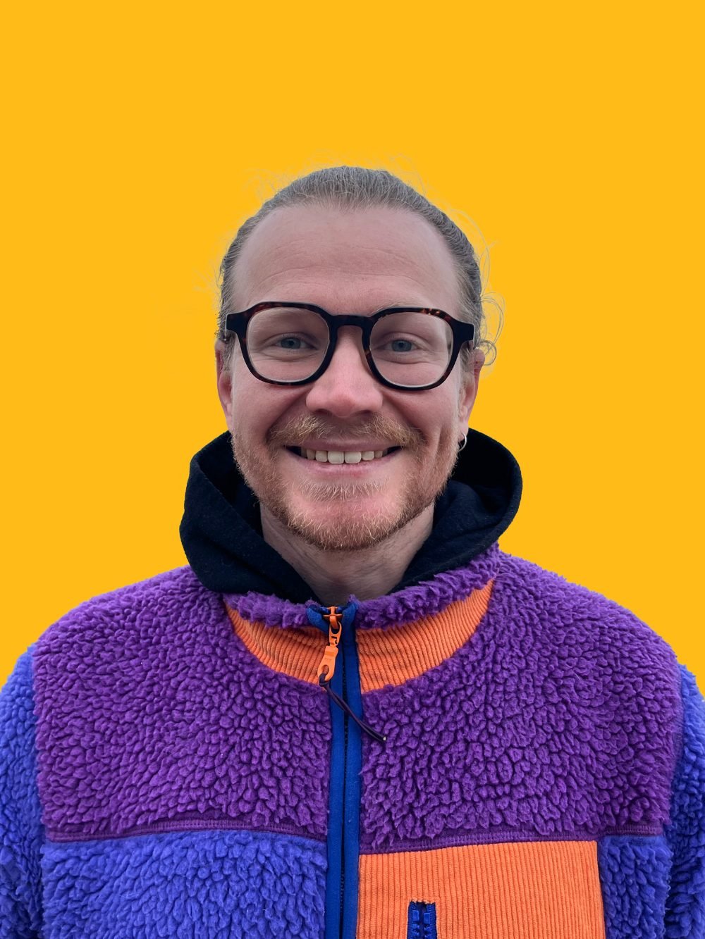 Portrait de Gaël Méhat, graphiste et directeur artistique à Quimper, souriant, lunettes et polaire violette, sur fond jaune.
